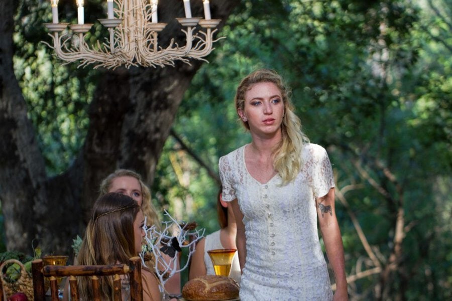 Performer in white lace dress stands at woodland table set with candelabra, bread, and wine during Branches music video shoot