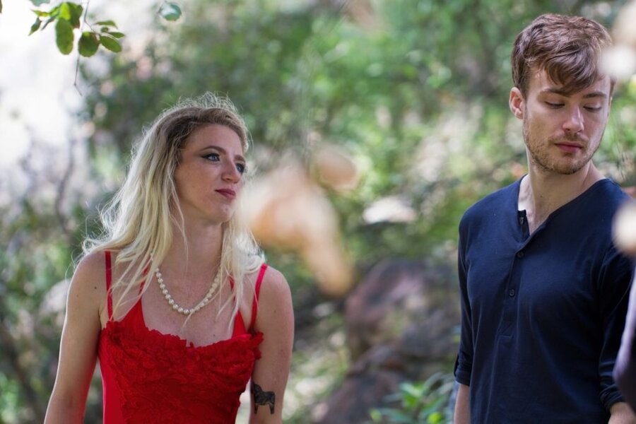 Woman in red dress with pearl necklace and man in navy shirt standing outdoors, Branches music video production