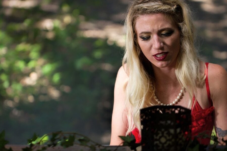 Blonde woman in red dress and pearl necklace reading script outdoors, Branches music video behind-the-scenes