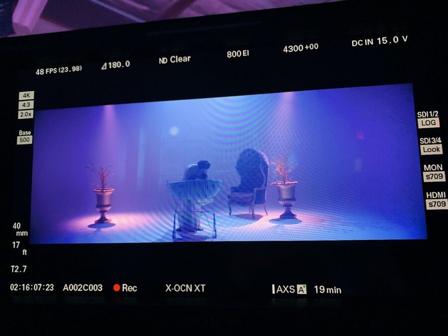 Director views monitor showing two silhouetted figures at table between candlesticks in atmospheric blue stage lighting