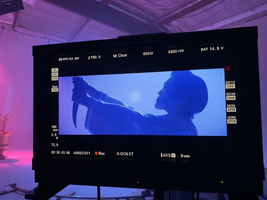 Large monitor displays blue-tinted scene during Tulsa Opera ad campaign shoot with purple ambient lighting.