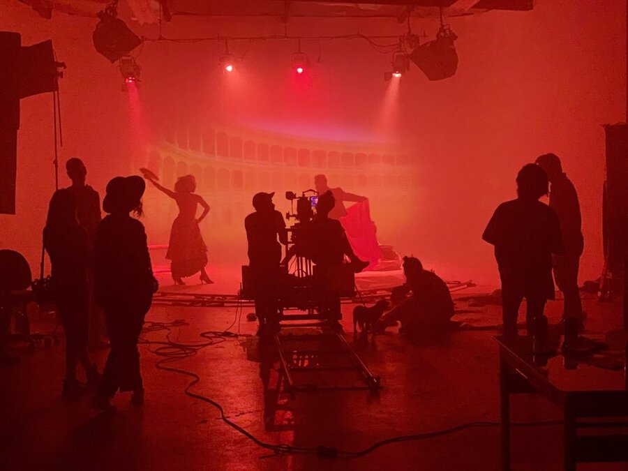 Film crew shooting in dramatic red-lit interior with haze, silhouettes of crew and equipment visible throughout space