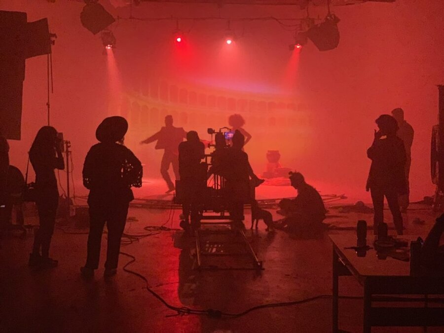 Film crew on set with intense red lighting and atmospheric haze during Tulsa Opera commercial shoot directed by James Kick...