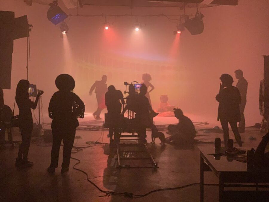 Film crew on hazy studio set with dramatic orange lighting and silhouetted figures during Tulsa Opera production
