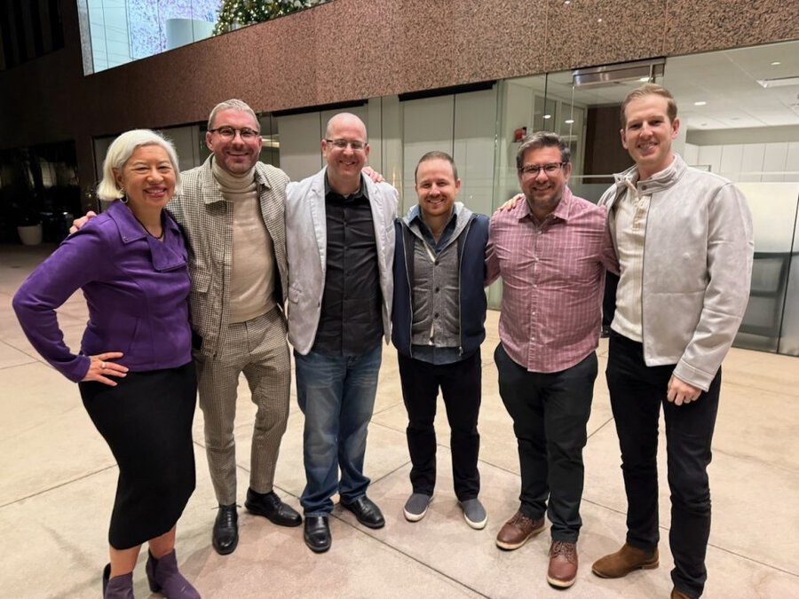Six professionals standing together in modern lobby with textured wall at United Talent Agency screening event
