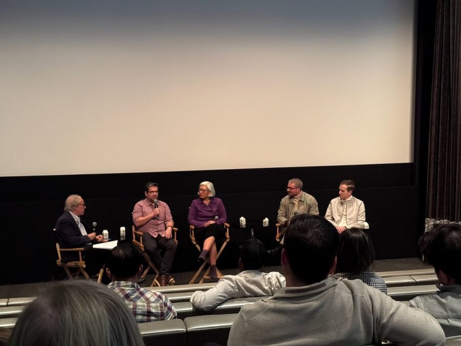Five panelists seated on stage at The American Question screening Q&A, theater interior with screen visible behind