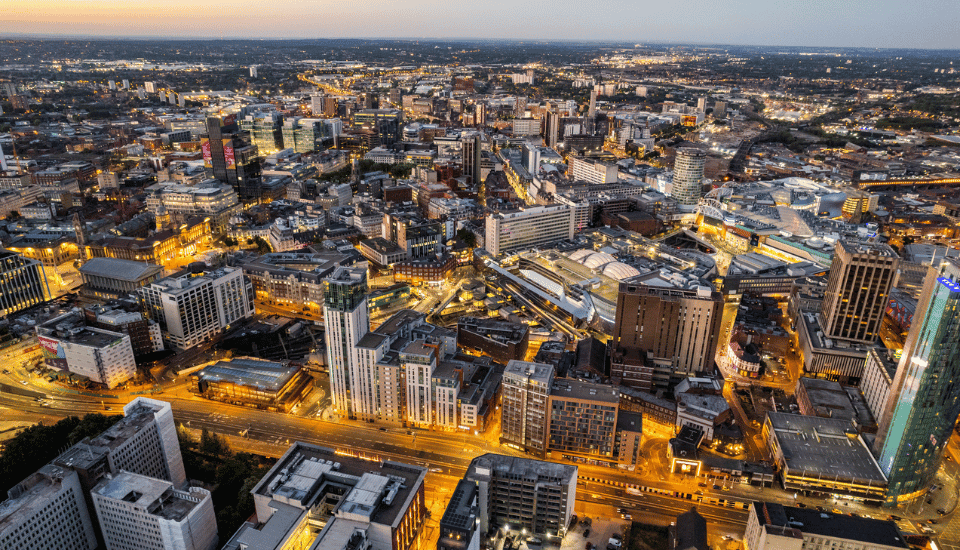 Aerial view of a city at dusk, with buildings, streets, and lights illuminating the urban landscape as daylight fades; a scene reflecting the vision of inclusive growth championed by the East Midlands Inclusive Growth Commission.