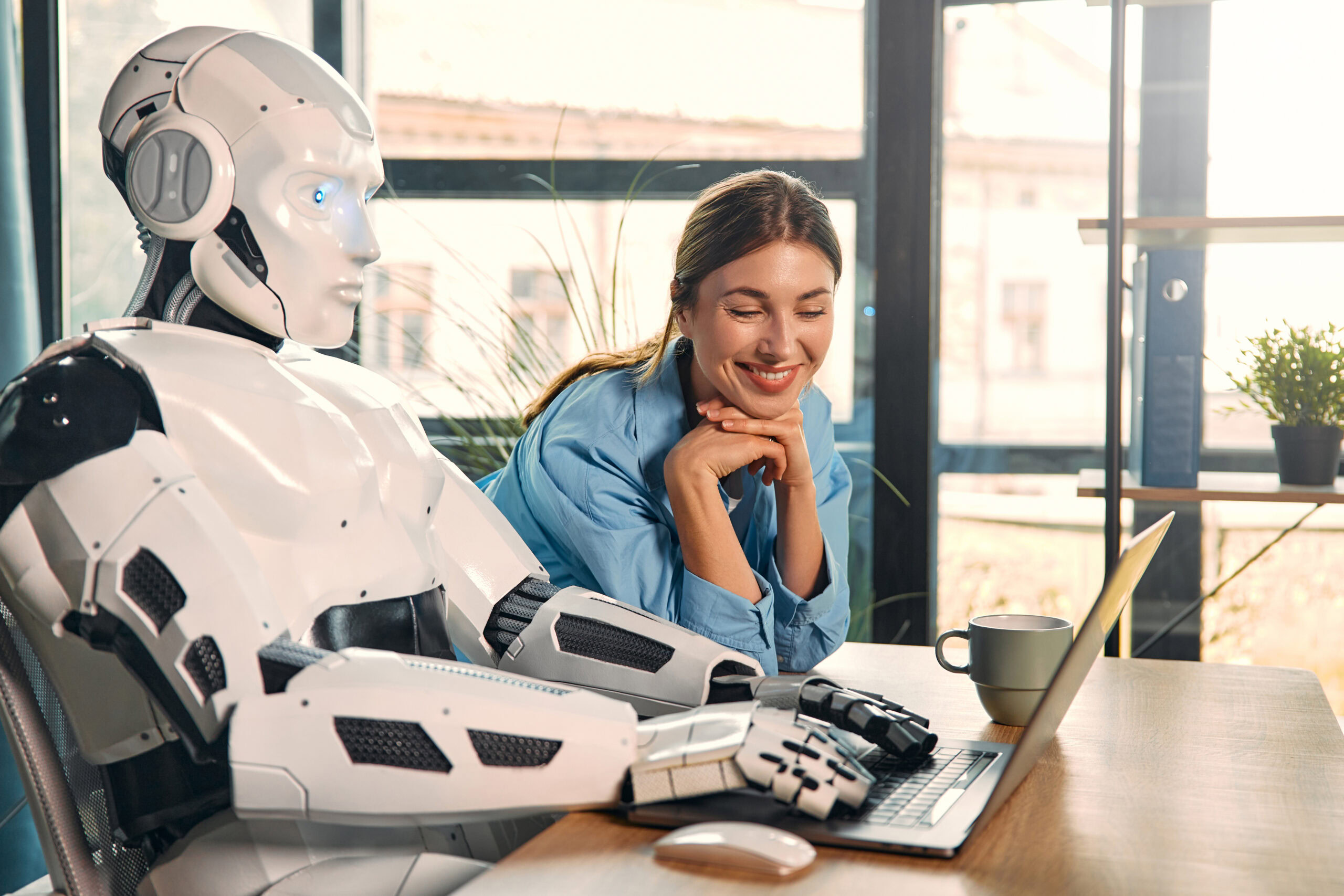 KI-Agententeam in der Praxis: Eine junge Frau arbeitet mit einem humanoiden Roboter an einem Laptop in einem modernen Büro und trinkt dabei Kaffee. Dies ist ein Beispiel für die Zusammenarbeit zwischen Menschen und künstlicher Intelligenz.