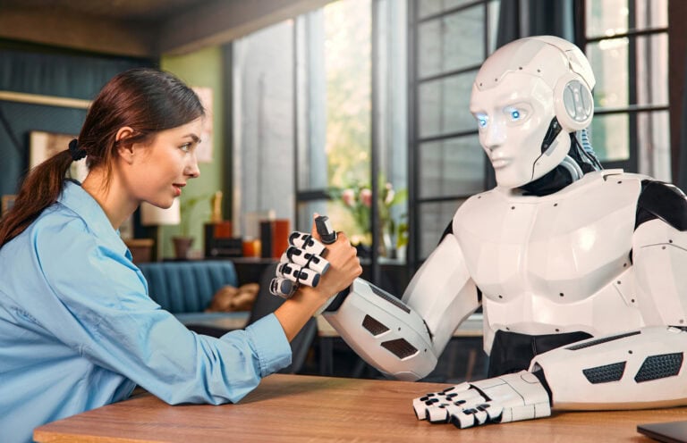Missverständnisse über KI-Agenten: Eine junge Frau und ein humanoider Roboter sitzen an einem Tisch in einem modernen Büro und spielen Armdrücken. Dies ist ein Beispiel für die Zusammenarbeit zwischen Menschen und künstlicher Intelligenz.