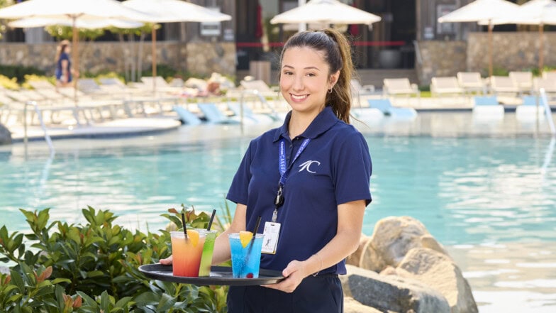 A server holding a tray of drinks in front of a pool.