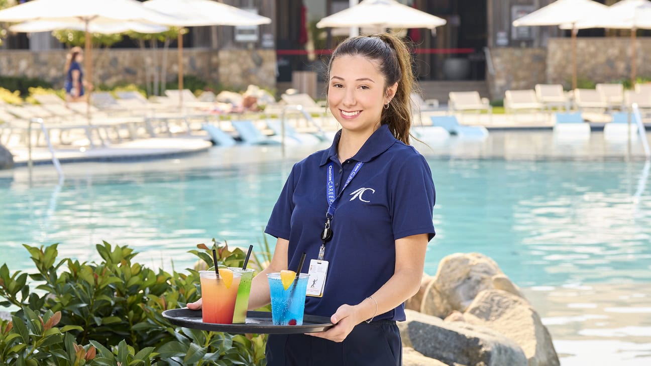 A server holding a tray of drinks in front of a pool.