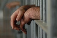 Mans hands behind bars in jail or prison