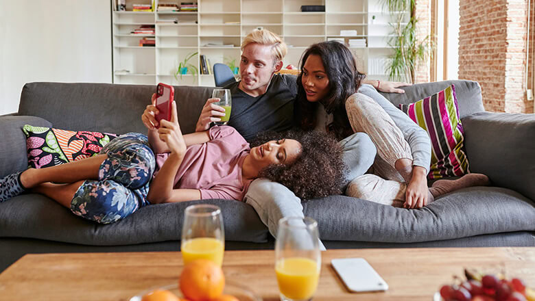 Relaxed family lounging on sofa, enjoying drinks and screen time at home.
