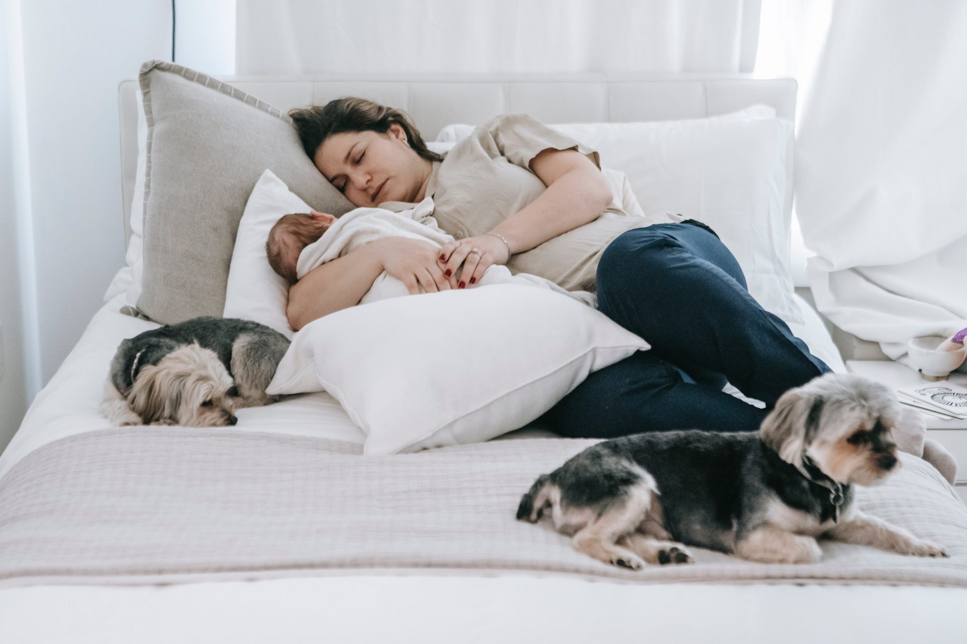 Young woman resting with newborn baby and dogs in bedroom, promoting debt relief and financial freedom.