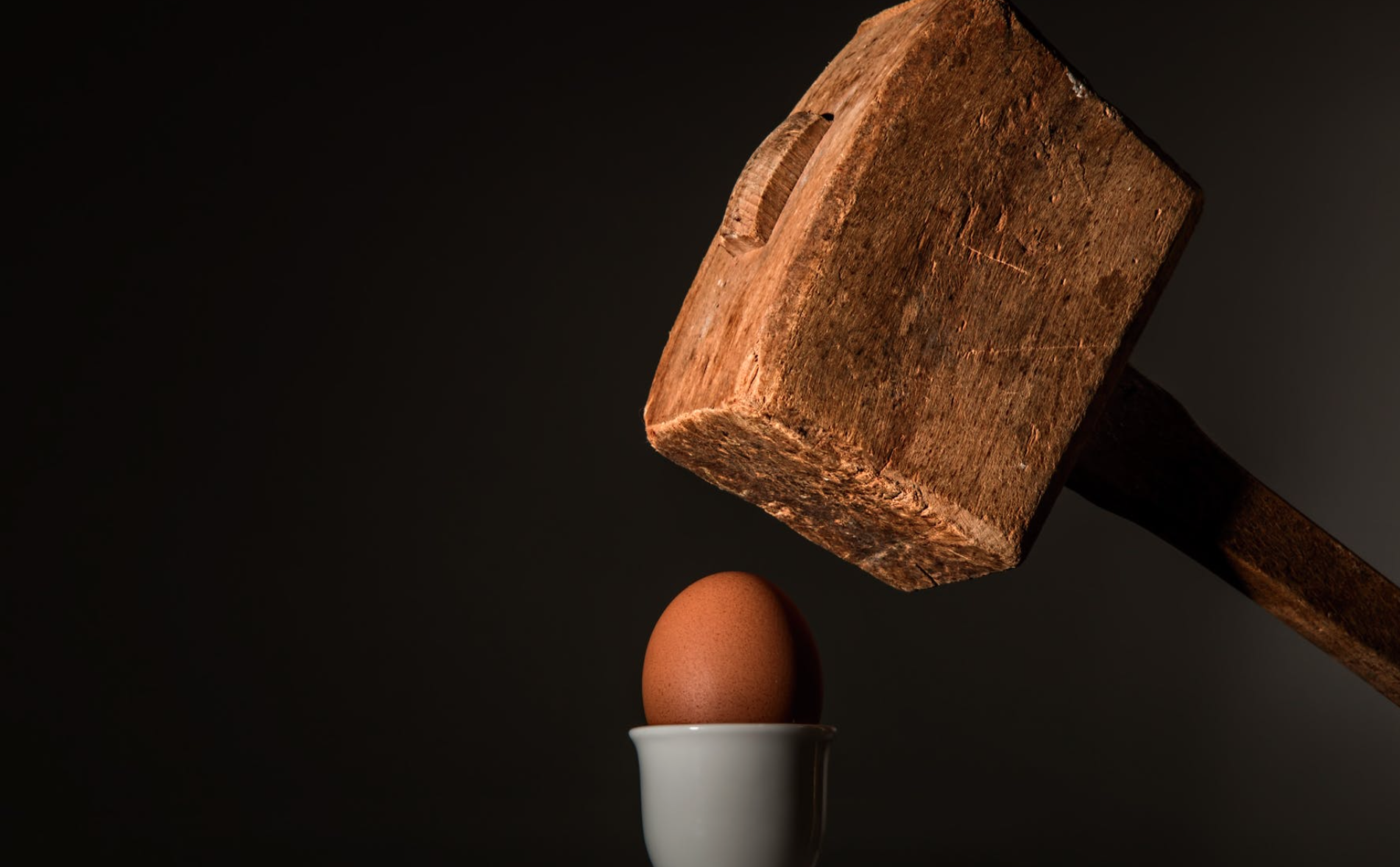 Crushing an egg with a wooden hammer for financial stress release or debt relief concept.