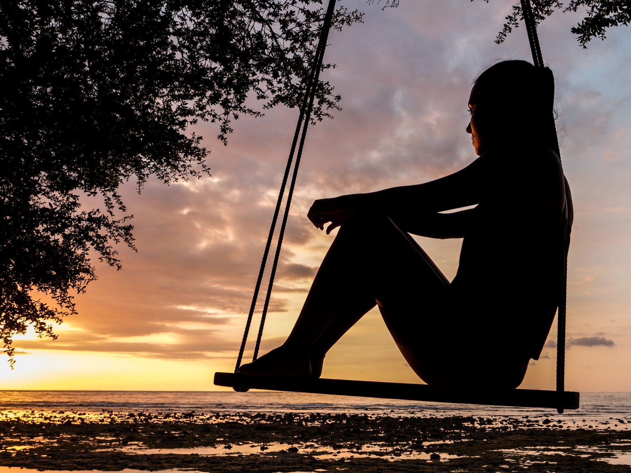 Silhouette of a woman on a swing at sunset, symbolizing hope and freedom from debt.
