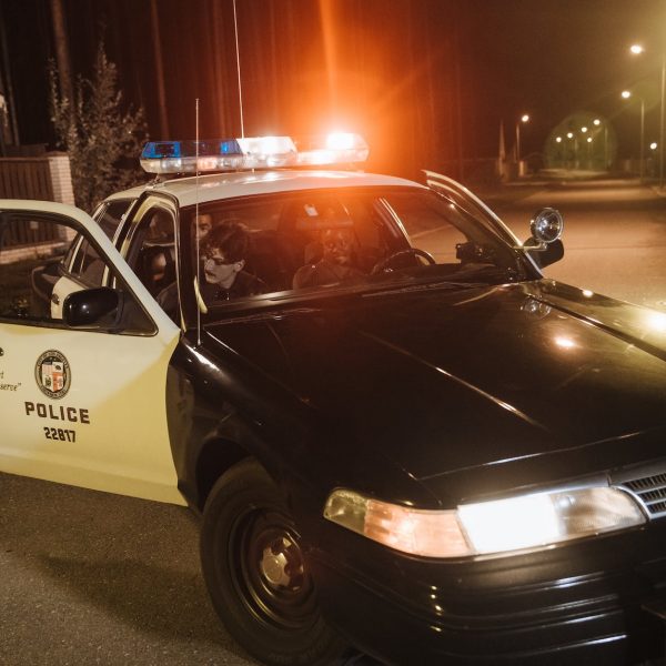 Police arrest scene at night with flashing lights, officers talking to suspects.