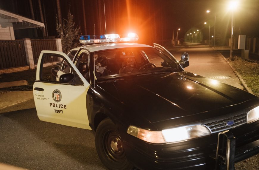 Police arrest scene at night with flashing lights, officers talking to suspects.