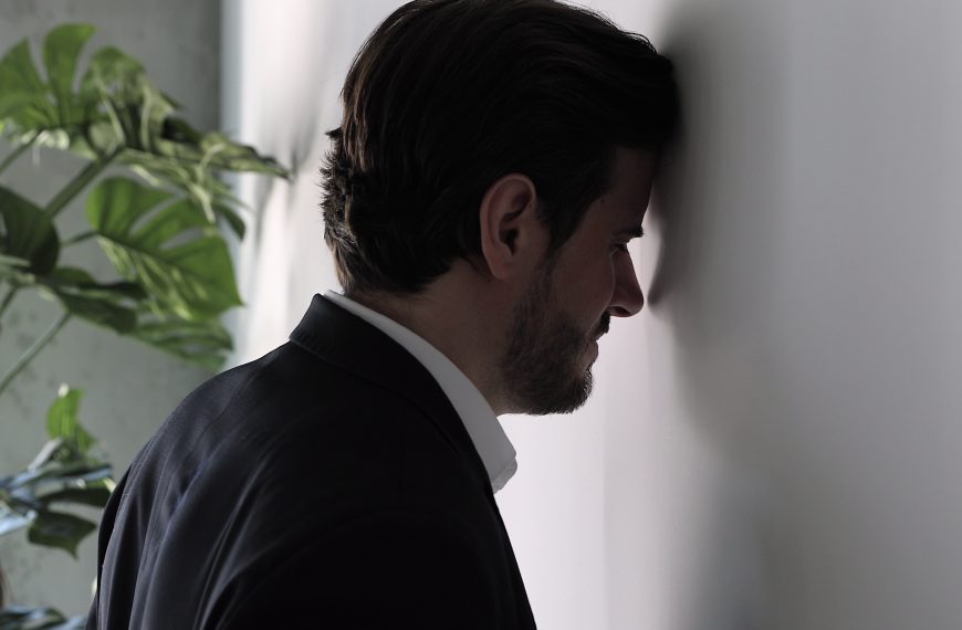 Overwhelmed man in a suit with head against the wall, stressed financial situation.