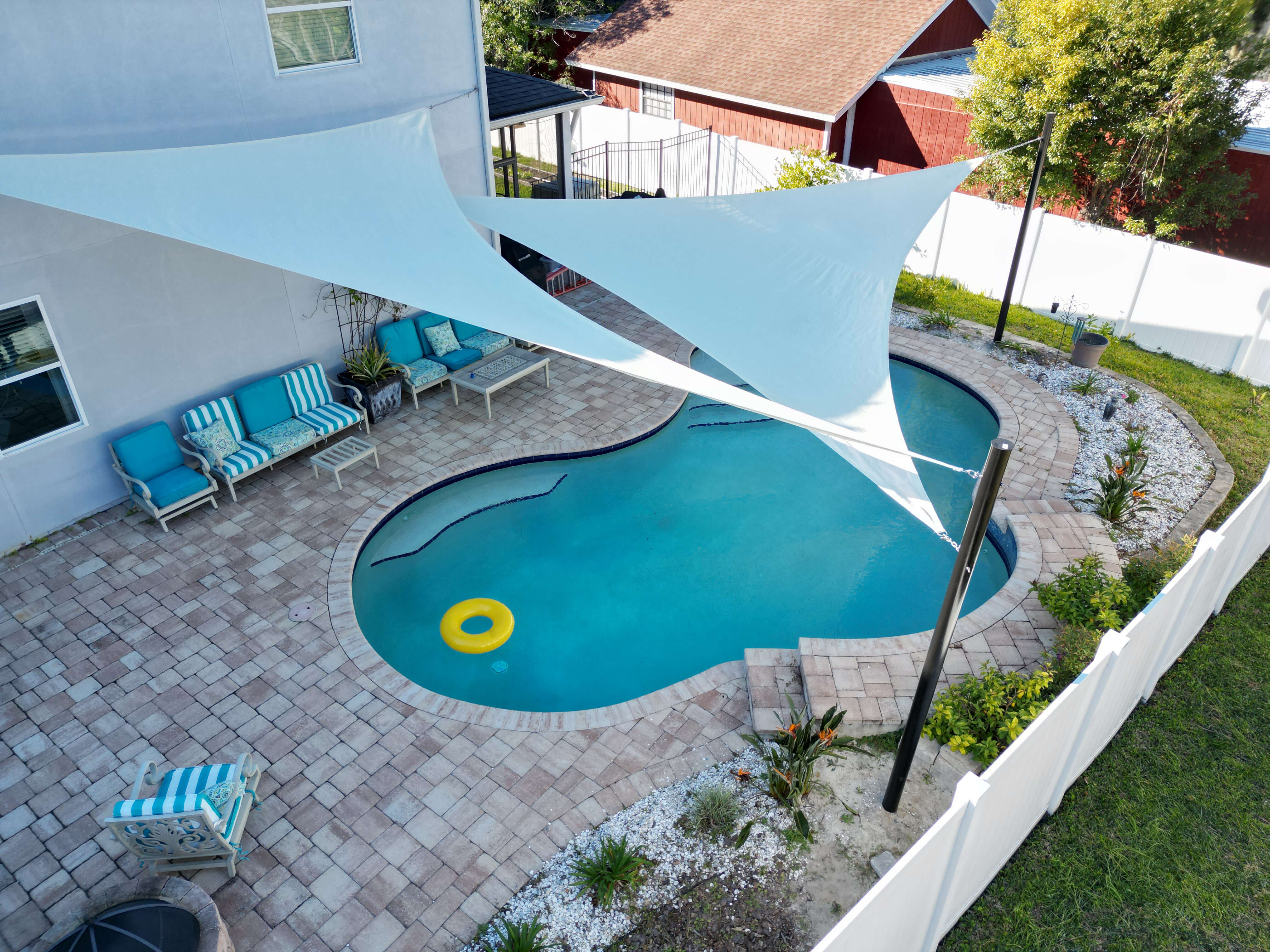 Get Summer Ready With Screen Enclosures and More Two beautiful triangle shade sails soar over top of a backyard pool, keeping our the direct sun.