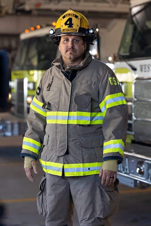 Jake Trujillo stands in front of fire trucks in his uniform