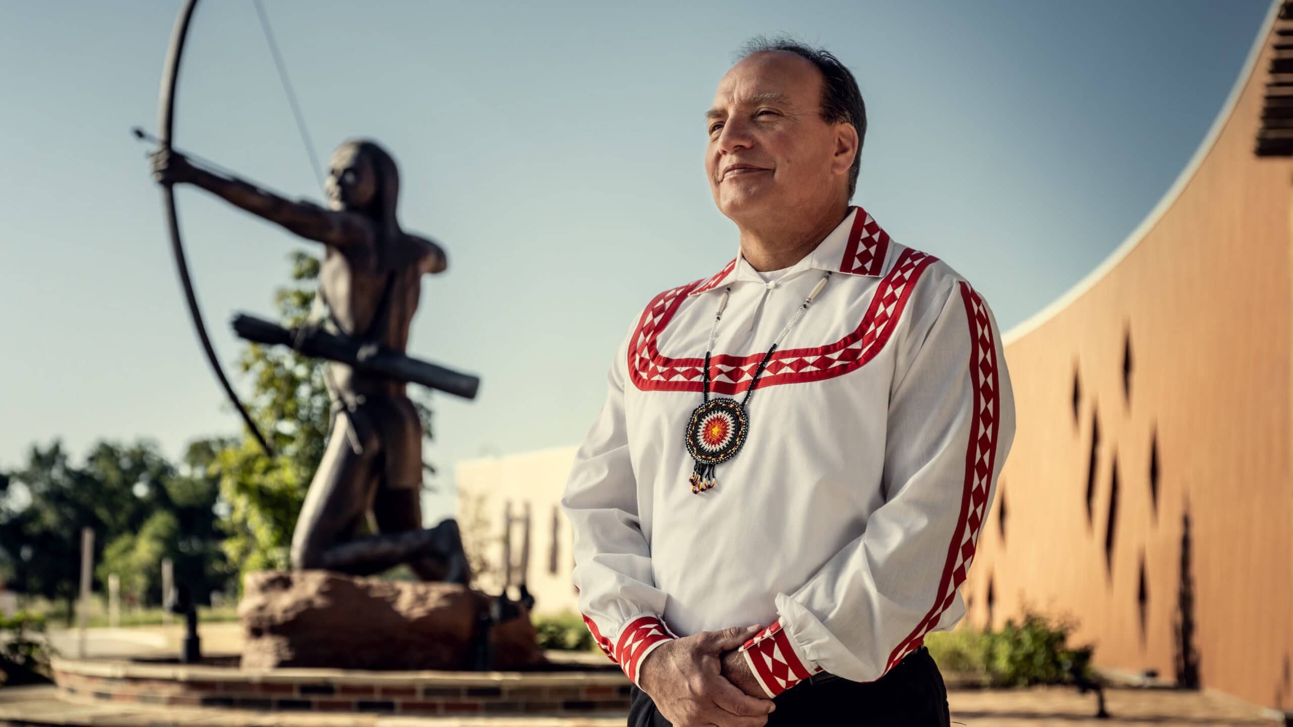 Gary Batton stands in front of a sculpture of Choctaw Warriors