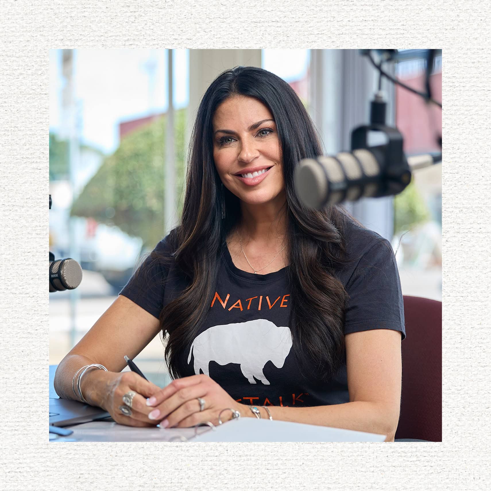 Rachael Yougman smiles at her podcasting desk, wearing a black shirt with a white bison on it