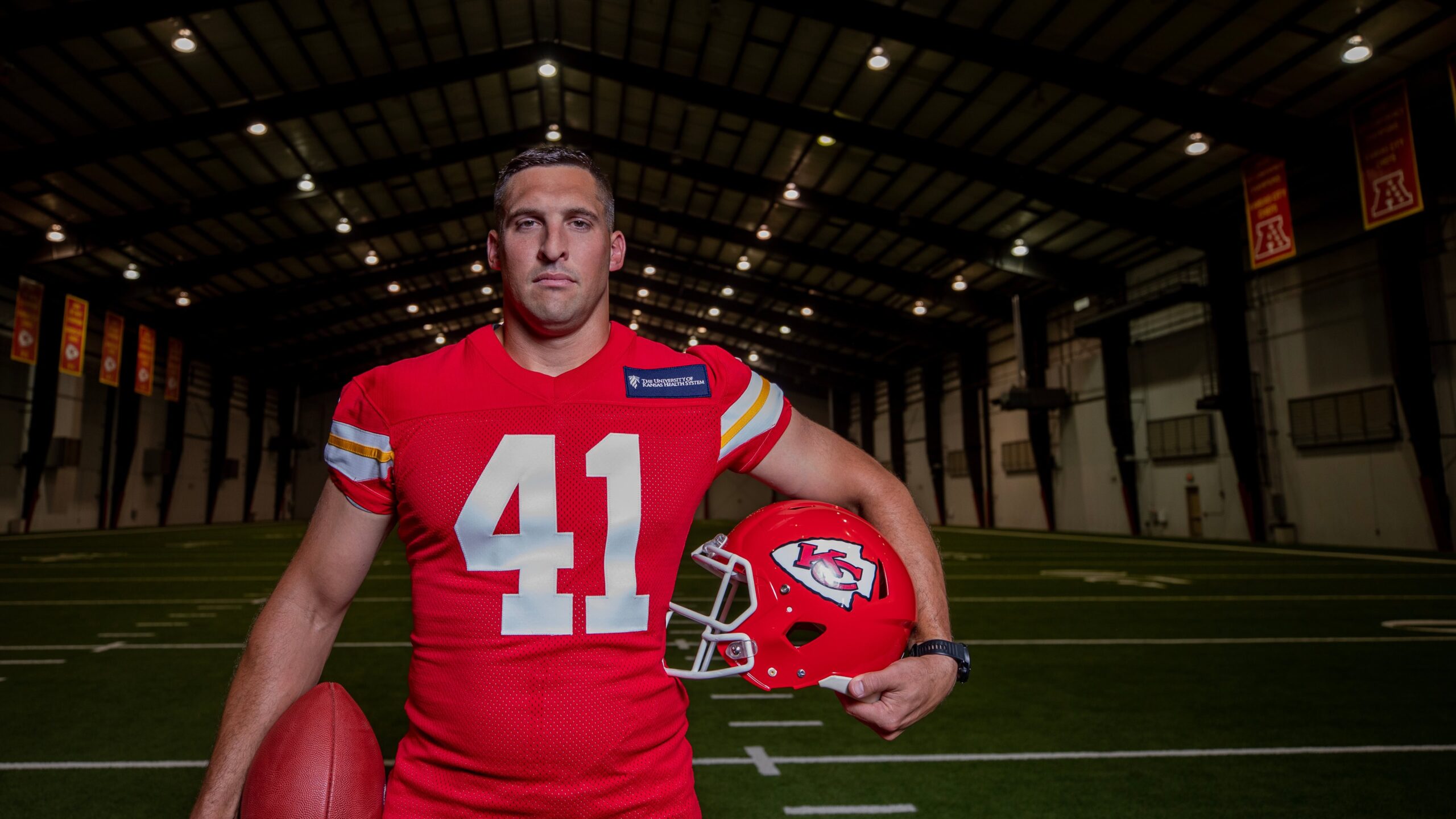 James Winchester holding football and KC Chief's helmet while wearing his jersey.