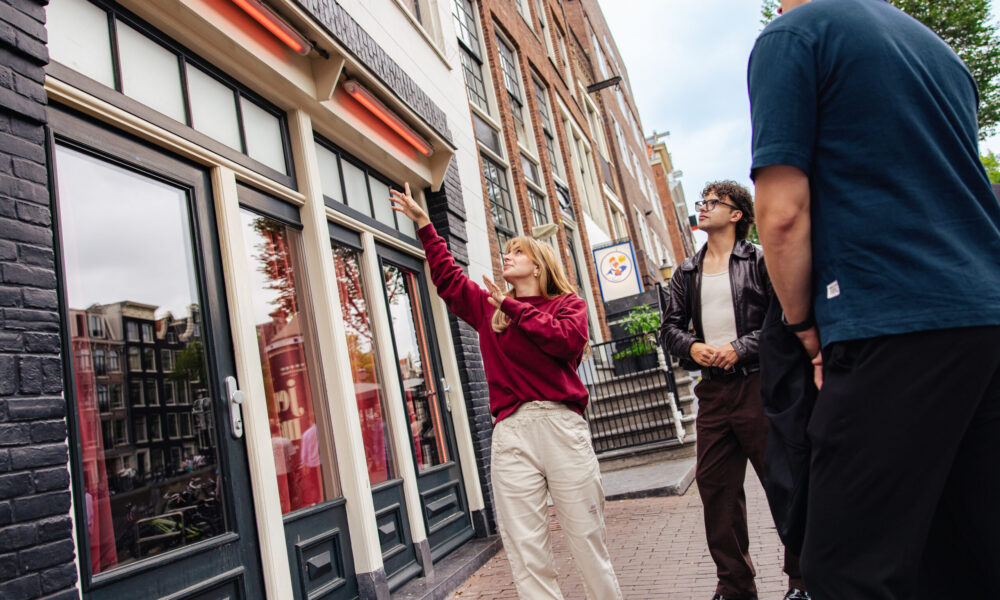 A guided small-group tour examines a distinctive historic building in Amsterdam. A guide in a red top points to architectural details for attentive participants.