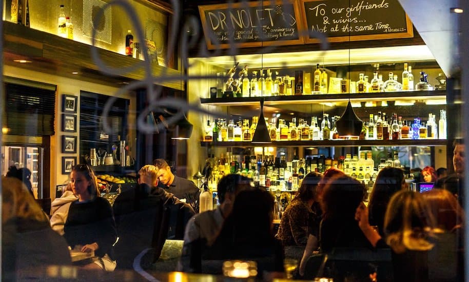 Menschen sitzen in der gemütlich, dunklen Atmosphäre in der Vesper Bar Amsterdam und genießen Cocktails.