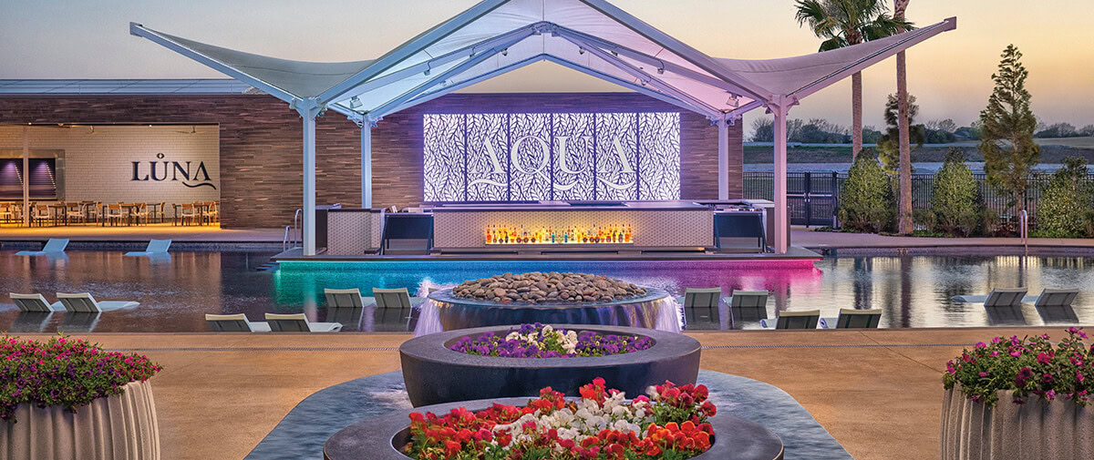 Poolside AQUA Bar with a sculptural canopy, illuminated backdrop, and water loungers, flower planters in the foreground.