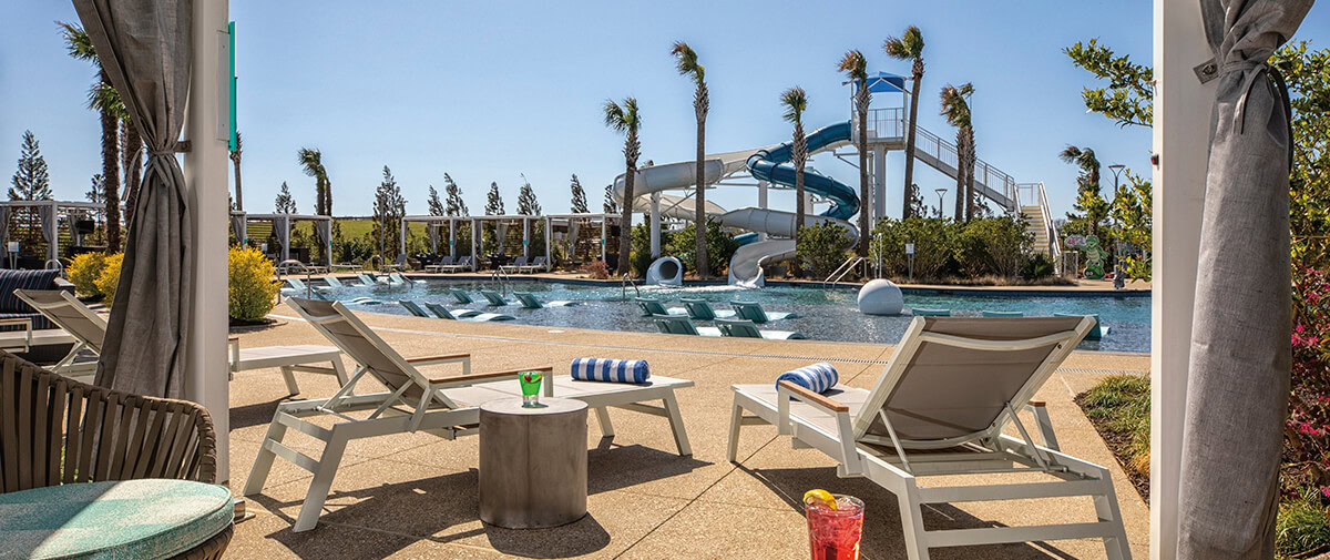 Resort pool with in-water loungers, palm trees, and a tall twisting waterslide; drinks on a small side table.