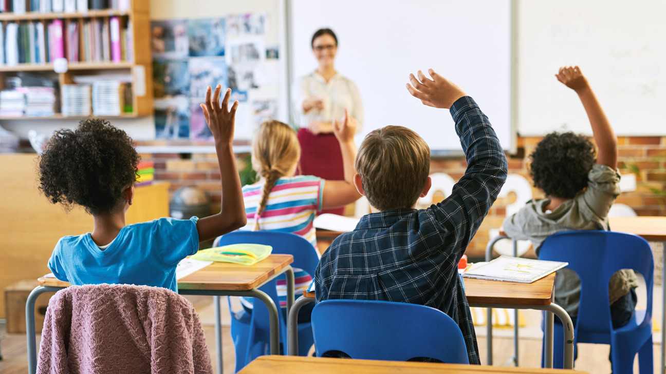 A group of students in a classroom with their hand raised.