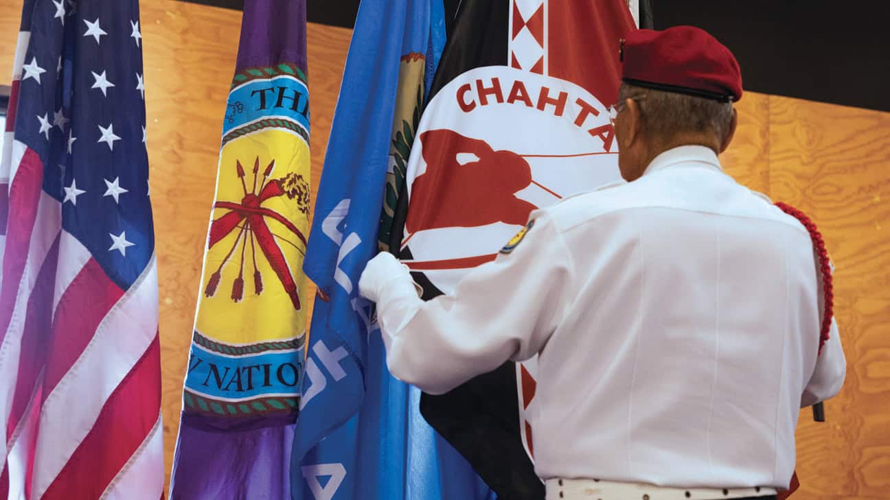 A Choctaw Veteran standing in front of flags.