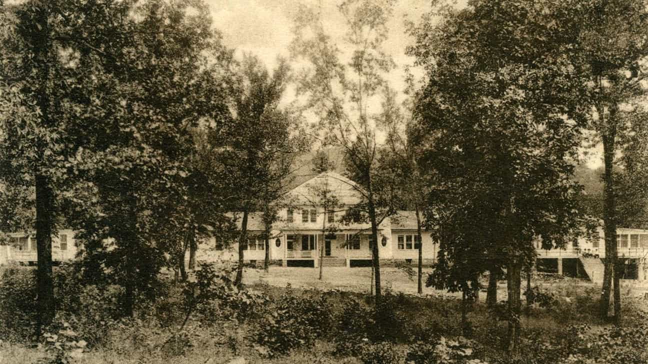 Black and white photo of the old Carter Hospital peaking through a line of trees. At the top middle of the photo it says, "View of Main Buildings, Carter Hospital, near Talihina, Okla.