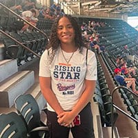 girl stands inside baseball stadium.