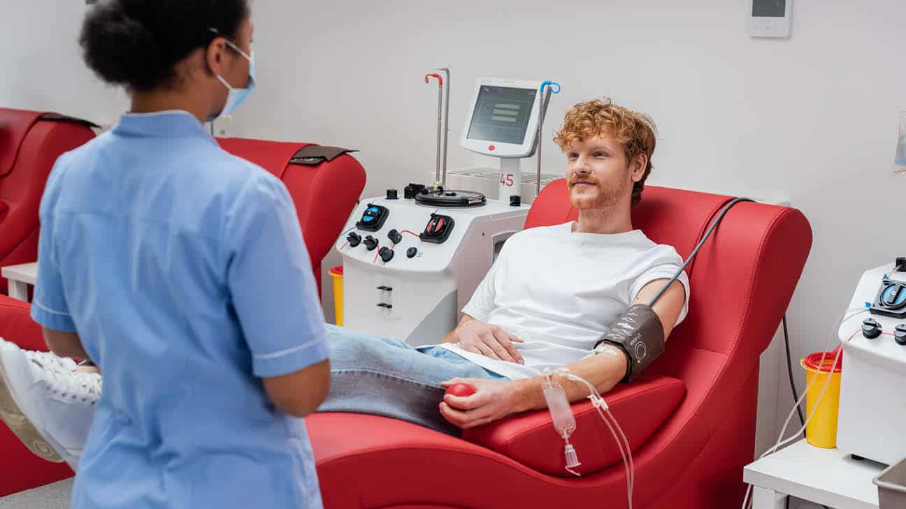 A person sitting in the chair talking to a nurse while donating blood.