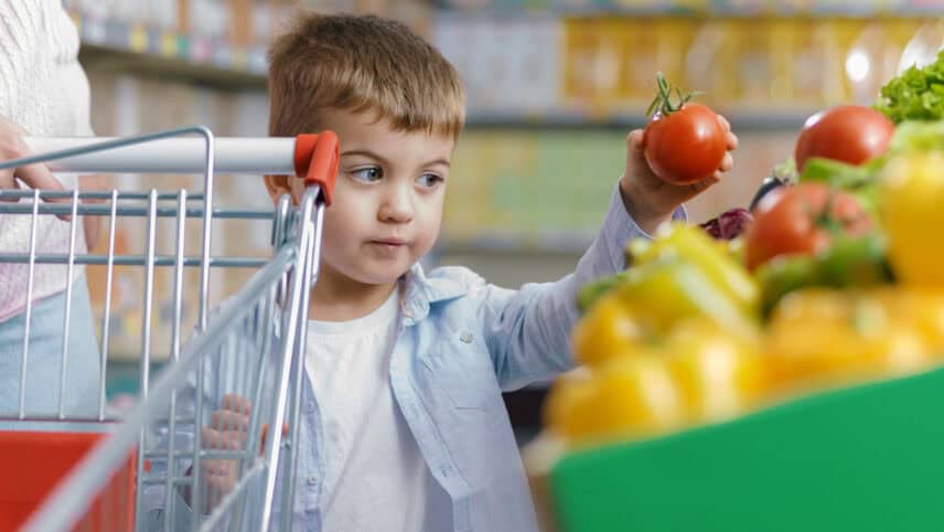Little boy grocery shopping picking out a red apple for the Summer EBT program