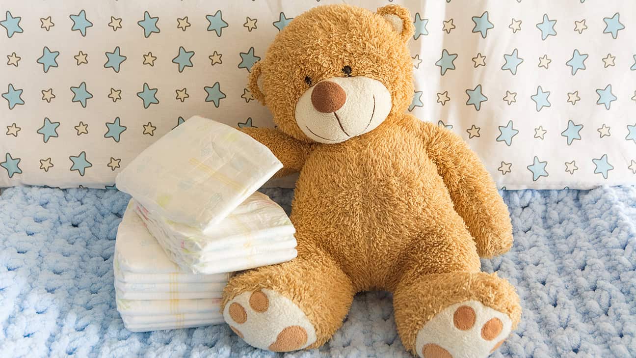 Diapers with baby soft toy bear on the background of the nursery and crib, the concept of using diapers for babies