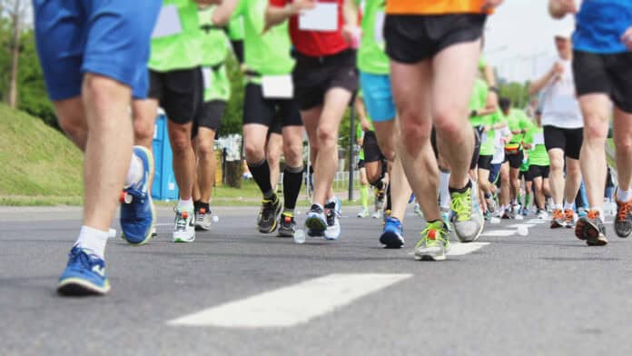 **Alt text:** Runners in athletic gear participating in a road race, with a focus on their legs and running shoes as they move down a city street.