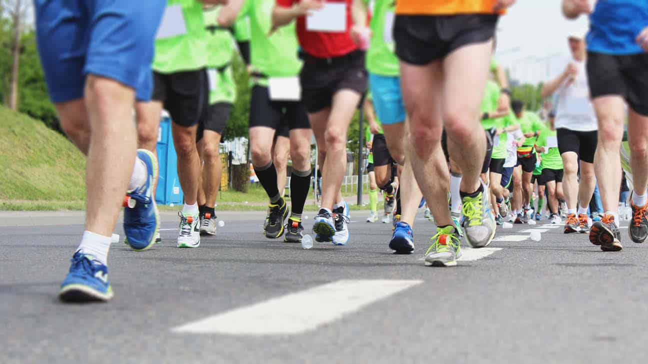 **Alt text:** Runners in athletic gear participating in a road race, with a focus on their legs and running shoes as they move down a city street.