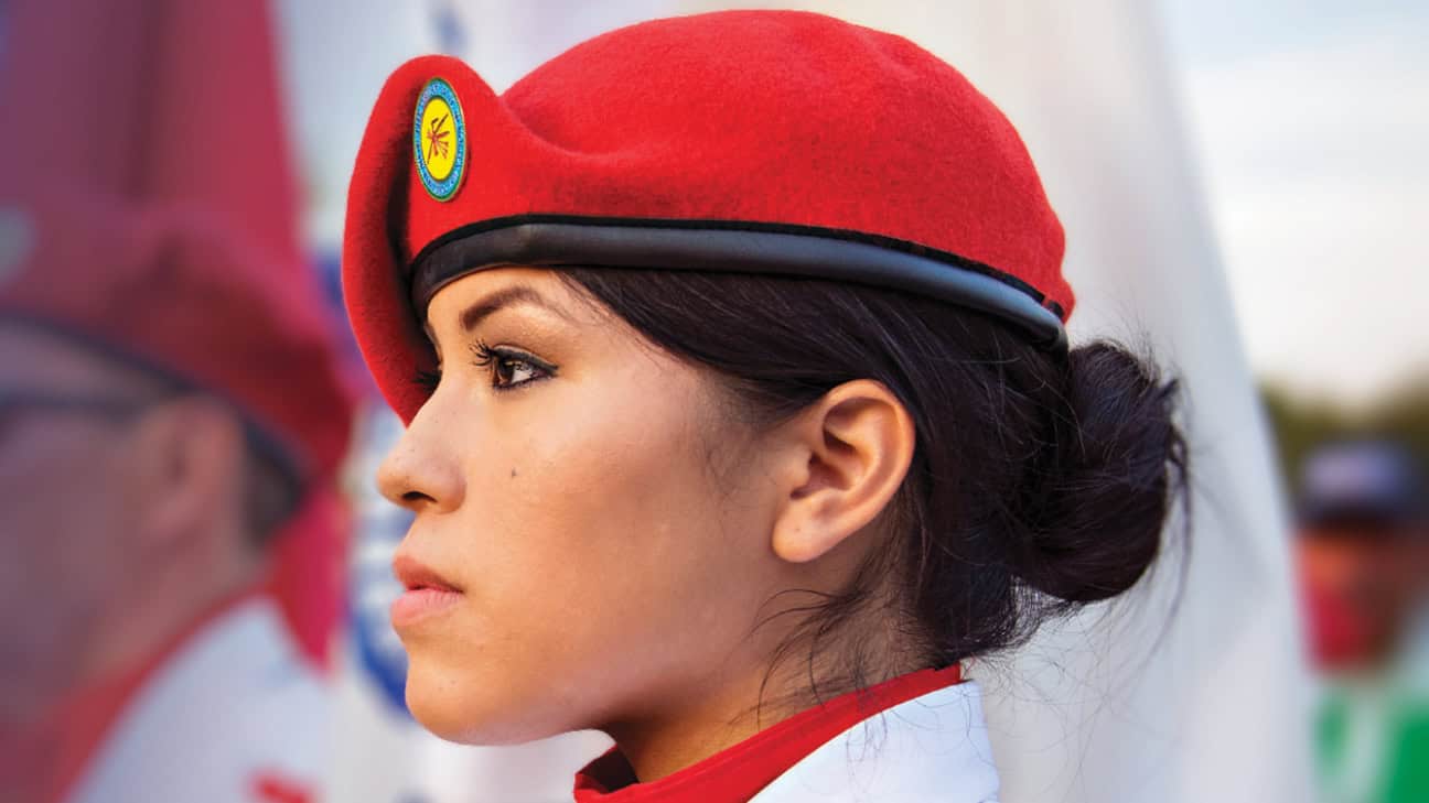 Young woman in a red military-style beret with an emblem patch, wearing a white uniform, looking forward with a focused expression.