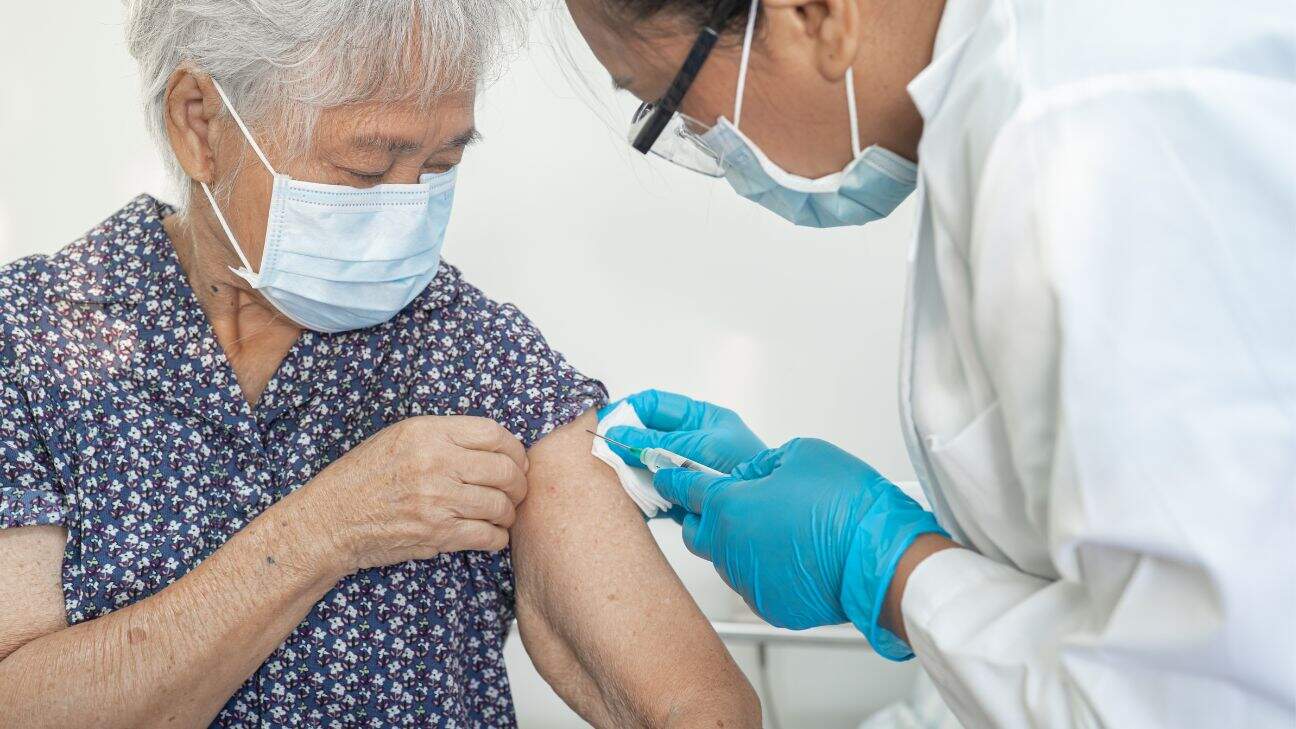 A doctor giving an elderly woman a shot in the arm.