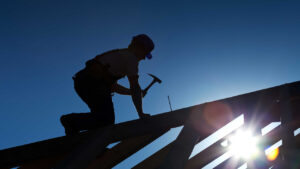 Worker hammering on top of a roof structure.