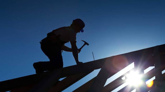 Worker hammering on top of a roof structure.