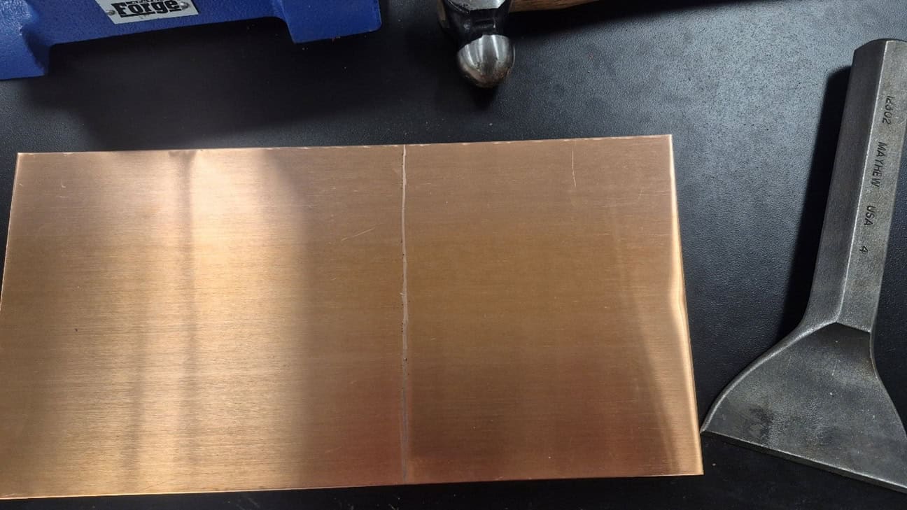 A metal hammer and chisel are used to cut off part of the copper sheer in preparation