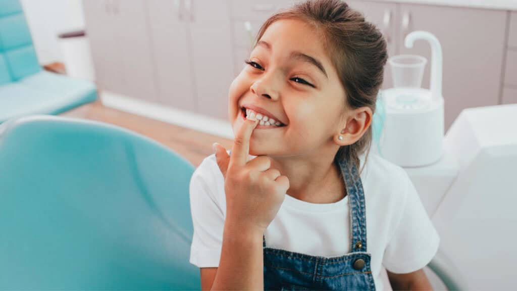 A child smiling and pointing to her teeth.