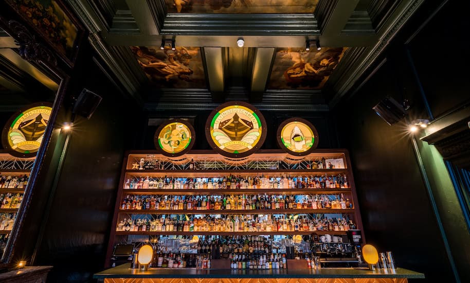 Barra oscura en la coctelería Flying Dutchman de Ámsterdam, con una pared llena de botellas para mezclar buenos cócteles.