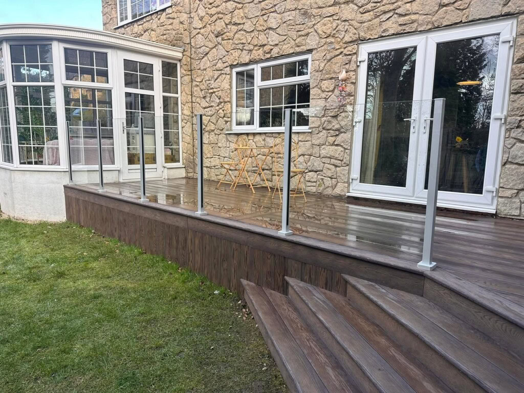 Raised Millboard deck with a glass balustrade against a stone house