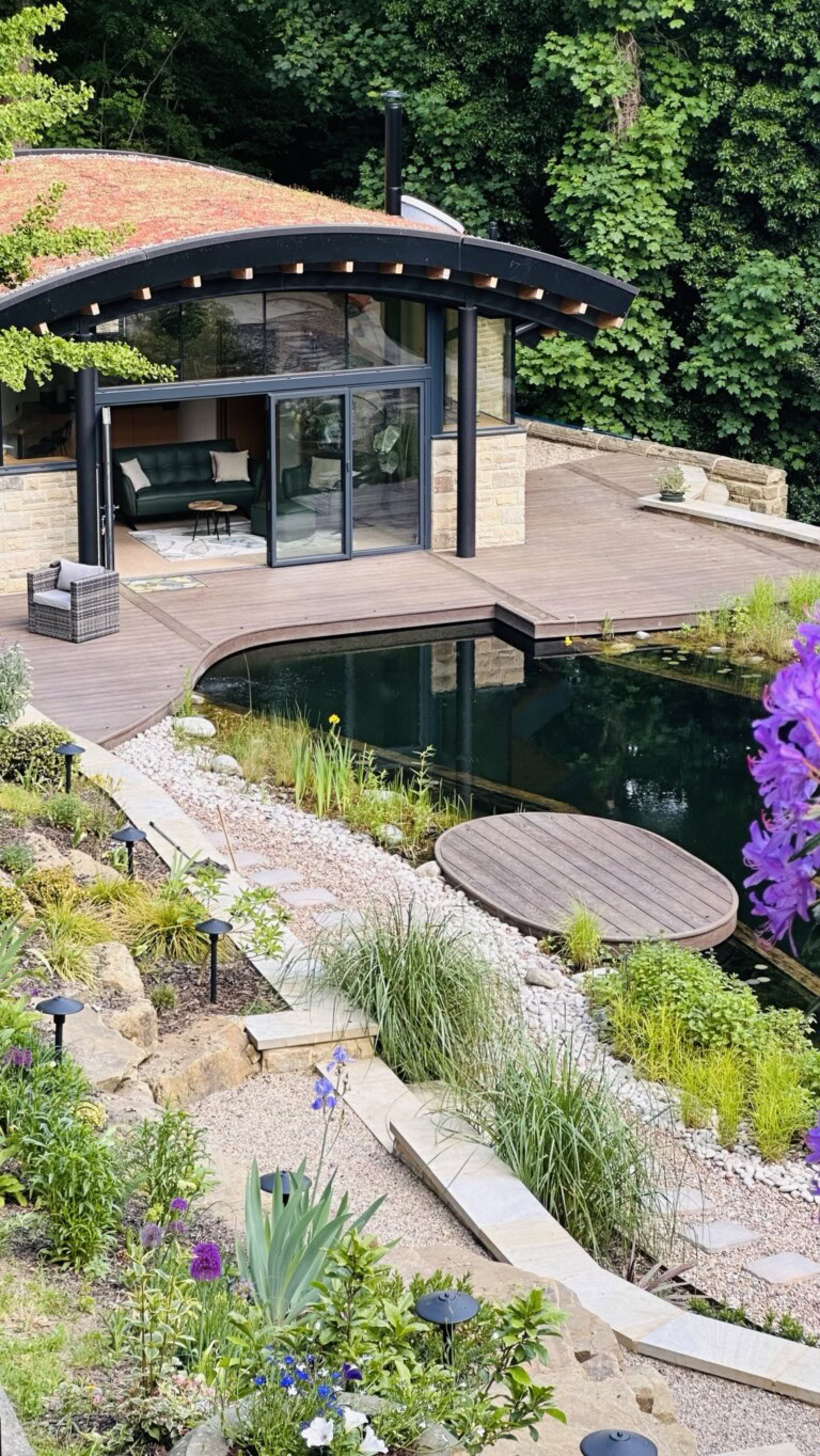 Millboard decking around a natural pool and a curved roof garden room